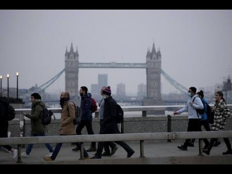 In this January 24, 2022 photo, workers walk over London Bridge towards the City of London financial district, backdropped by Tower Bridge, during the morning rush hour, in London.