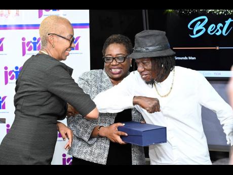Best Groundsman awardee Denis Reid of St Andrew Primary School greets Education Minister Fayval Williams with an elbow bump as Mona Sue-Ho, senior manager of social development at the Jamaica Social Investment Fund, looks on.