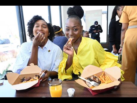 Social media influencers Arianne Logan (left) and Jodi-Ann Tucker dig into Island Grill’s festive feast of jerk chicken, signature seasoned fries and festivals.