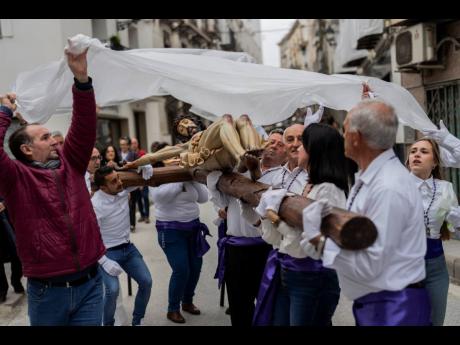 Members of the “Vera Cruz” Catholic brotherhood cover a figure of Jesus Christ with a plastic sheet to protect it from the rain, during a Holy Week procession in the southern town of Quesada, Spain.