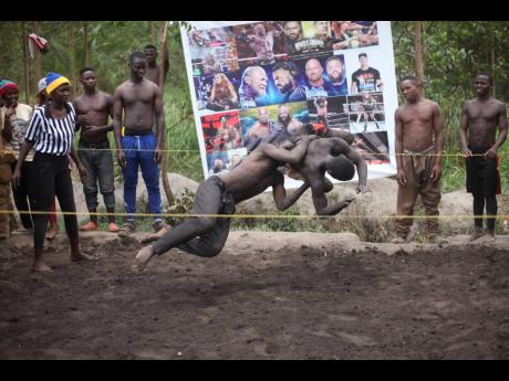 Ugandan youth perform an amateur wrestling tangle in the soft mud in Kampala.