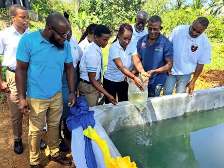 Leonardo Crossbourne (fourth left), head boy of Maldon High School in St James, joins Georgia Scarlett (centre), environmental coordinator of the Sandals Foundation, in pouring small fish into the school’s newly unveiled fish tank during the vessel’s c