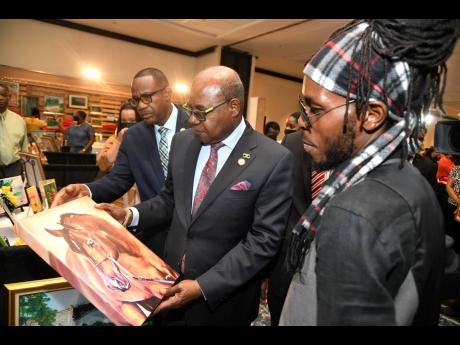 Fine Artist, Delroy Millwood, shows off his art work to Edmund Bartlett, (centre) minister of Tourism and David Dobson, chief technical director of the Ministry of Tourism at the 8th staging of the Christmas in July tradeshow at  Jamaica Pegasus Hotel, on 