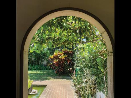 An arched wall opening frames a garden fish pond.