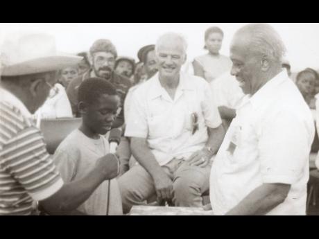 In this 1984 photo, Patrick McFarlane (second left) of Manchester is seen presenting to National Push-cart Derby patron, Governor General Sir Florizel Glasspole, an album consisting of photographs of previous push cart derbies, at the National finals at Di