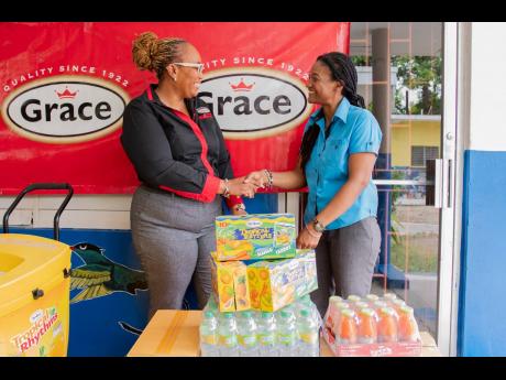 Angella Wander (left), consumer services manager at Grace Foods, shakes hands with Sarah Birthwright-Forskin, principal of Holy Trinity Basic School, during a visit on April 18 as part of Grace Foods’ breakfast initiative aimed at treating students and t