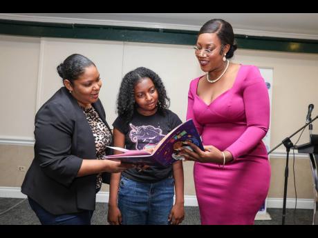 Author and STEM advocate, Dianne Plummer (right), shows Dr Natwaine Gardner, principal director, science, Ministry of Science, Energy, Telecommunications and Transport, and her daughter, Jade Stewart, the pages of her newly launched STEM children’s book,
