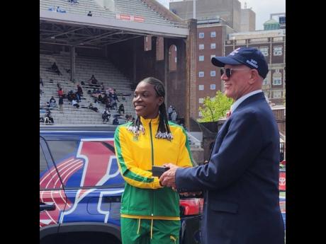 Jade-Ann Dawkins (left) of St Jago High collects her Penn Relays commemorative watch from a meet official yesterday after retaining the high school girls’ Championship of  America triple jump title with a leap of  13.01 metres