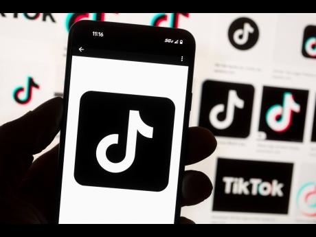 The TikTok logo is displayed on a mobile phone in front of a computer screen. 