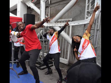 Usain Bolt (left), multiple Olympic and World Championship gold medallist, pulls out his signature pose with two Red Stripe dancers during the launch of Red Stripe’s ‘Guh Fi Gold and Glory’ campaign at the Half-Way Tree Transport Centre yesterday.