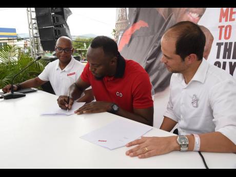 Sean Wallace (left), head of commerce, Red Stripe, and Daaf Van Tilburg (right), managing director, Red Stripe, look on as Usain Bolt, multiple Olympic and World Championship gold medallist, signs a contract to become brand ambassador for Red Stripe during