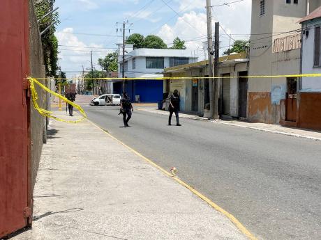 Police patrol the cordoned off area where the disabled Toyota Isis motor car, in which the alleged gunmen were travelling who engaged police in a shootout, crashed at the intersection of Charles and King Streets in downtown Kingston yesterday. Four men wer