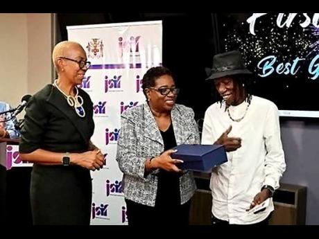 Fayval Williams (left), minister of education and youth, and Mona Suho, of the Jamaica Social Investment Fund, present an award to groundsman Denis Reid.