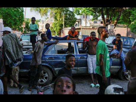 Youth hang out near cars serving as street barricades, placed there by residents to deter gangs from entering their neighborhood, in downtown Port-au-Prince, Haiti, on Friday, May 17.