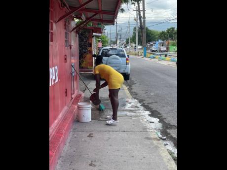 A woman cleaning the bloodstained concrete pavement in front of a bar along Collie Smith Drive in St Andrew, where tragedy unfolded on Tuesday night as journalist Job Nelson was murdered.