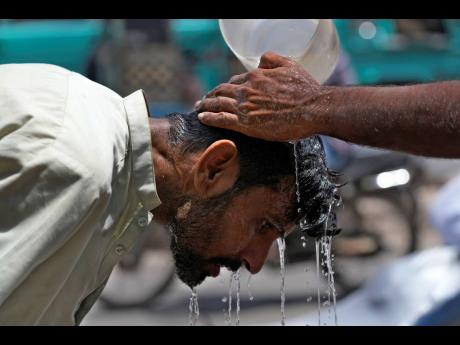 A volunteer pours water over the head of a man to cool off himself during a hot summer day in Karachi, Pakistan, Tuesday, May 21.
