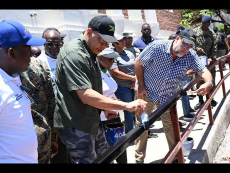 Prime Minister Andrew Holness (third left) and Opposition Leader Mark Golding paint the railing along a ramp at the National Labour Day project at the Institute of Jamaica in downtown Kingston on Thursday. Looking on (from left) are Pearnel Charles Jr, min