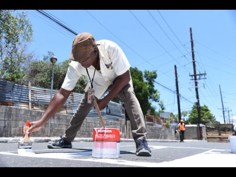 A resident of Greenwich Road in Arnett Gardens, St Andrew, paints a pedestrian crossing in his community for Labour Day on Thursday.