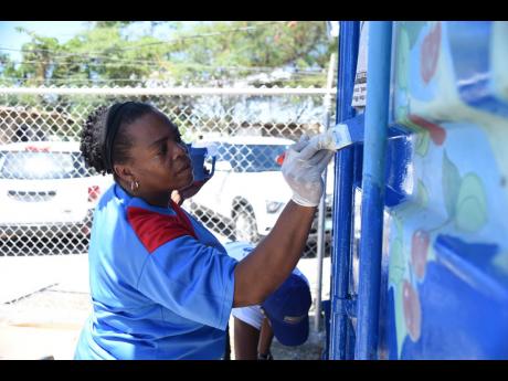 left: Michelle Dixon, vice-principal of Laura’s Basic School in Duhaney Park, St Andrew, brightens up the façade of the kitchen at the school with the help of JN Fund Management, which executed its Labour Day project at the institution.