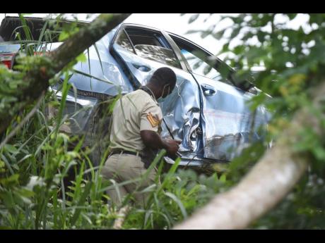 An accident scene investigator examines the wreckage of the vehicle in which Kevin O. Smith and a policeman sustained injuries along Church Road, in the vicinity of the Linstead Bypass, on October 26, 2021. Both Smith and Constable Orlando Irons succumbed 