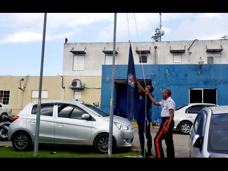 Policemen raise the Jamaica Constabulary Force flag at halfmast in honour of the late Constable Orlando Irons at the Freeport Police Station in Montego Bay on October 26, 2021, a day after he and disgraced pastor Kevin O. Smith succumbed to crash-related i