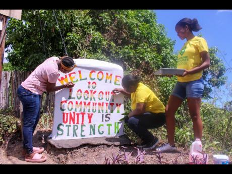 ‘Supreme Hero’ Anesha Miller joined Chloleen Daley-Muschett, corporate communications and PR manager of Supreme Ventures Limited, and her daughter Gia Baijnath in painting the welcome sign in the Look Out Community last Thursday as part of Labour Day a