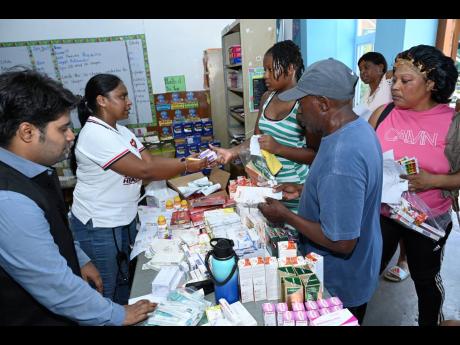Anuj Kumar Verma (left), of the Indian High Commission to Jamaica, and Dr Alekya Daram, of Ashish Health Care Centre, hand out medication to residents of Rae Town in Kingston at the High Commission of India 34th medical camp.