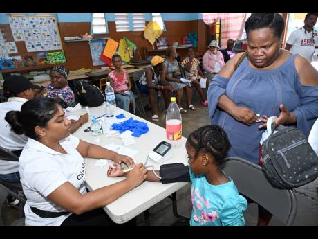 Nurse Matilda Arava (left), of Ashish Health Care Centre, checks Mackayla Grizzle’s blood pressure while her mother, Taniesh Manley, looks on.