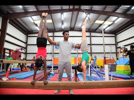 Coach Daniel Williams assists Emma-Marie Donaldson (left) and Leah Cowan (right) in correcting their form whilst practising handstands.