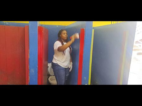 Lifespan Spring Water Bottling Company’s executive assistant Jessica Hartley assists in painting the boys’ bathroom at Buff Bay Primary School on Tuesday.