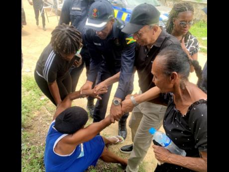 Minister of National Security Dr Horace Chang (third left) and Area One police commander, Senior Superintendent Glenford Miller (second left) assist in lifting a grieving Marlene Nation from the ground as she mourned the death of her son and grandson.
