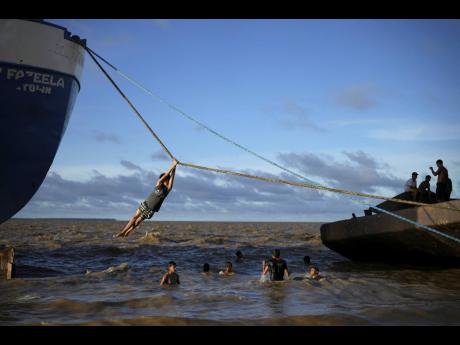 A child rappels over a stretch of the Essequibo River, using the rope of a ship docked in Parika, Guyana.