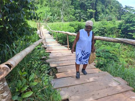 Icylin Robinson, an elderly resident of Cowick Park, Manchester, carefully crosses a makeshift wooden bridge a few metres from the collapsed Troy bridge.