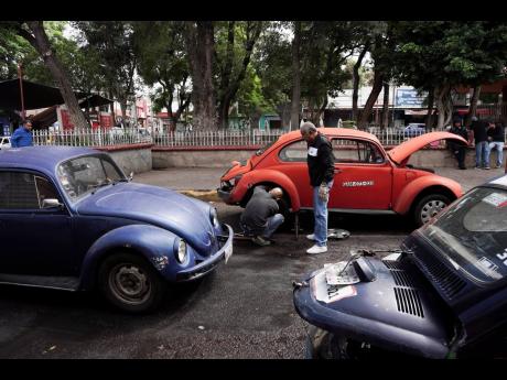 Volkswagen Beetle taxi drivers change a flat tyre in the Cuautepec neighbourhood of Mexico City.