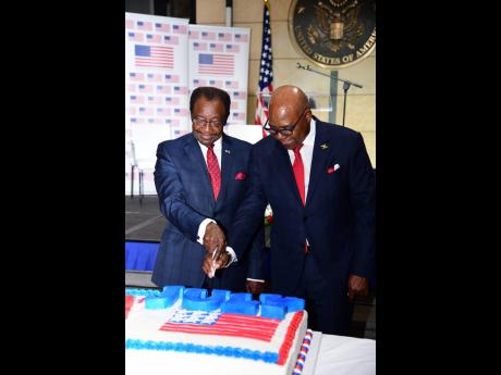 Ambassador N. Nick Perry (left) and Tourism Minister Edmund Bartlett indulge in the age-old tradition of cutting the ‘birthday’ cake. 