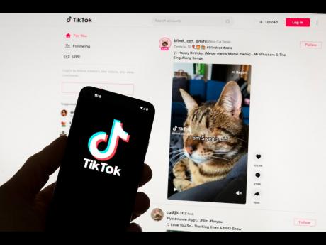 The TikTok logo is seen on a mobile phone in front of a computer screen which displays the TikTok home screen.