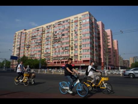 Chinese riding bicycle pass by a local business building in the background in Beijing, China, Friday, June 28, 2024. Surveys of Chinese factory managers showed a mixed outlook for the world’s second-largest economy in June, with growth steady but not pic