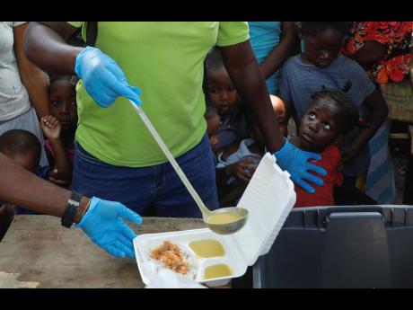 A server ladles soup into a container as children line up to receive food at a shelter for families displaced by gang violence, in Port-au-Prince, Haiti, on March 14.