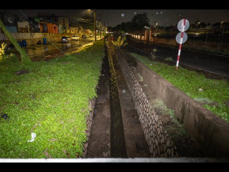 The gully which runs along Collie Smith Drive in St Andrew as seen on Wednesday night. It is alleged that 20-year-old Alrick Moncrieffe (inset) jumped into the gully to retrieve a football and was swept away by the rushing waters.
