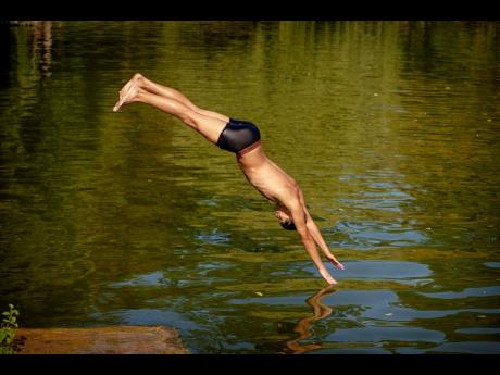 A boy jumps in a lake in Bucharest, Romania, Tuesday, July 9, 2024, as temperatures exceeded 39 degrees Celsius (102.2 Fahrenheit). The national weather forecaster issued a orange warning for the coming week, as temperatures are expected to reach 40 degree