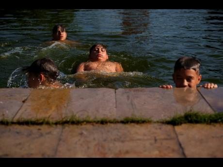 Boys cool off in a lake in Bucharest, Romania, Tuesday, July 9, 2024, as temperature exceeded 39 degrees Celsius (102.2 Fahrenheit). The national weather forecaster issued an orange warning for the coming week, as temperature is expected to reach 40 degree