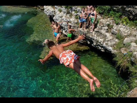 A boy dives into the Cijevna river near Montenegro's capital Podgorica, as temperatures soared to 36 degrees Celsius (96.8 Fahrenheit) on Thursday, July 11, 2024. Weather alerts, forest fires, melting pavement in cities: A sizzling heat wave has sent tempe