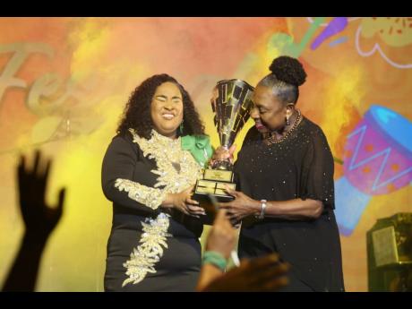 Kimiela 'Candy' Isaacs (left) is presented with the first place trophy after winning the 2024 Jamaica Festival Song Competition with '#One Jamaica'. 