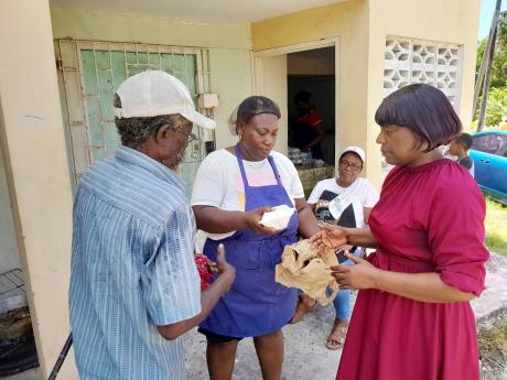 Pastor of the Hopewell Church of God of Prophecy, Veronica Clark (right), with the assistance of a volunteer, handing a lunch prepared under the post-Hurricane Beryl church feeding programme to a senior citizen from Hopewell, Hanover.