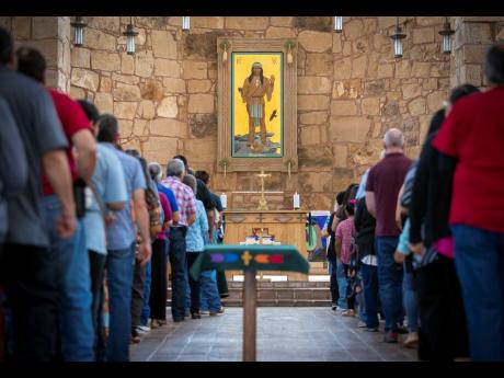 Mescalero Apache Tribe members and parishioners wait in line to receive Communion during a Mass at the St Joseph Apache Mission church in Mescalero, New Mexico on Sunday, July 14. Behind the altar is the Apache Christ painting, an icon that depicts Christ 