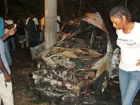 A woman views the burnt remains of a Toyota Fielder motor car which crashed in Runaway Bay, St Ann, killing one person several years ago.