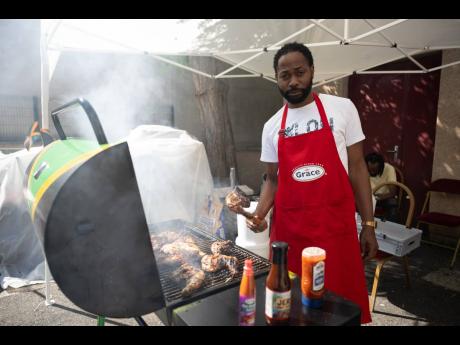 Omar Robinson assists Wayne Smith (not pictured), a restaurateur and caterer, with preparing jerked chicken outside Jamaica House in Paris to keep the patrons satisfied during their visit yesterday.