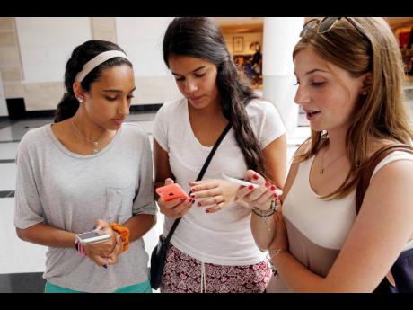 Isabella Cimato, 17, from left, Arianna Schaden, 14, and Sofia Harrison, 15, check their phones at Roosevelt Field shopping mall in Garden City, N.Y., on July 27, 2015.