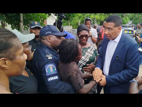 Prime Minister Andrew Holness consoles Debbie-Ann Hamilton Francis who lost three family members in a drive-by shooting in Cherry Tree Lane, Four Paths, Clarendon.