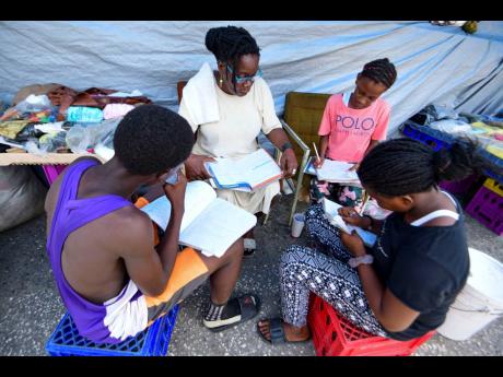 Suzette Williams, a vendor on Sutton Street for the past 10 years, assists Marissa Nelson (foreground, right), Latonya Rennie (background, right)), and Jordaine O’Connor (left) with their studies at her stall last Tuesday.